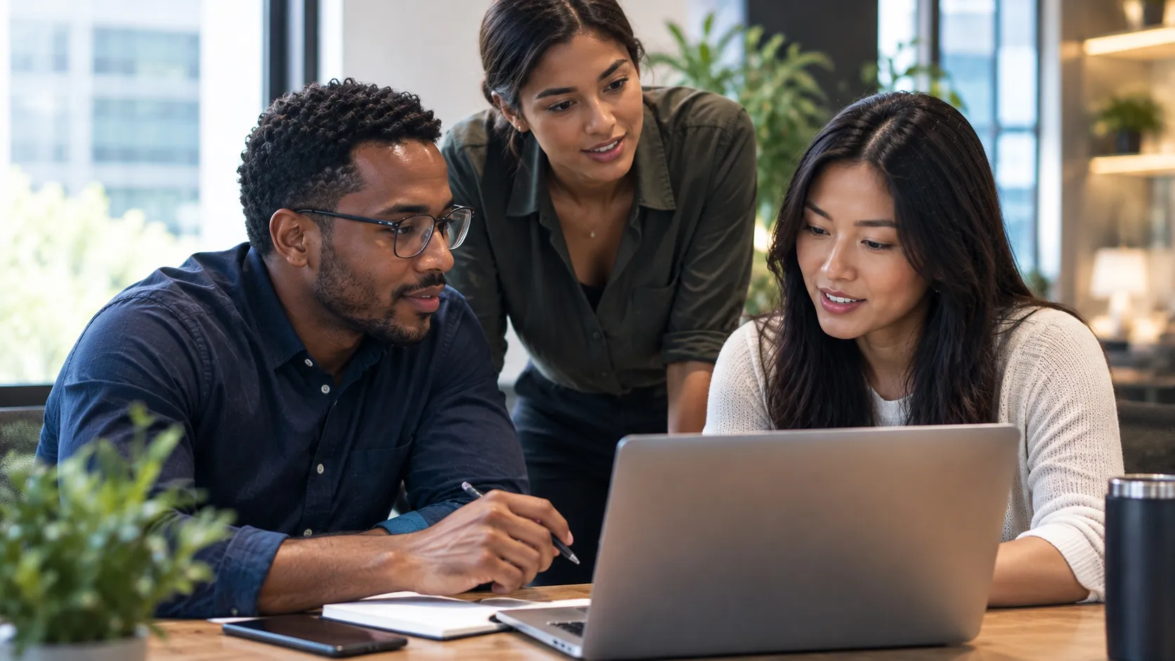 Three professionals collaborate around a laptop in a modern office, illustrating secure information sharing, effective business communication, and teamwork to protect confidential information and support better business decisions.