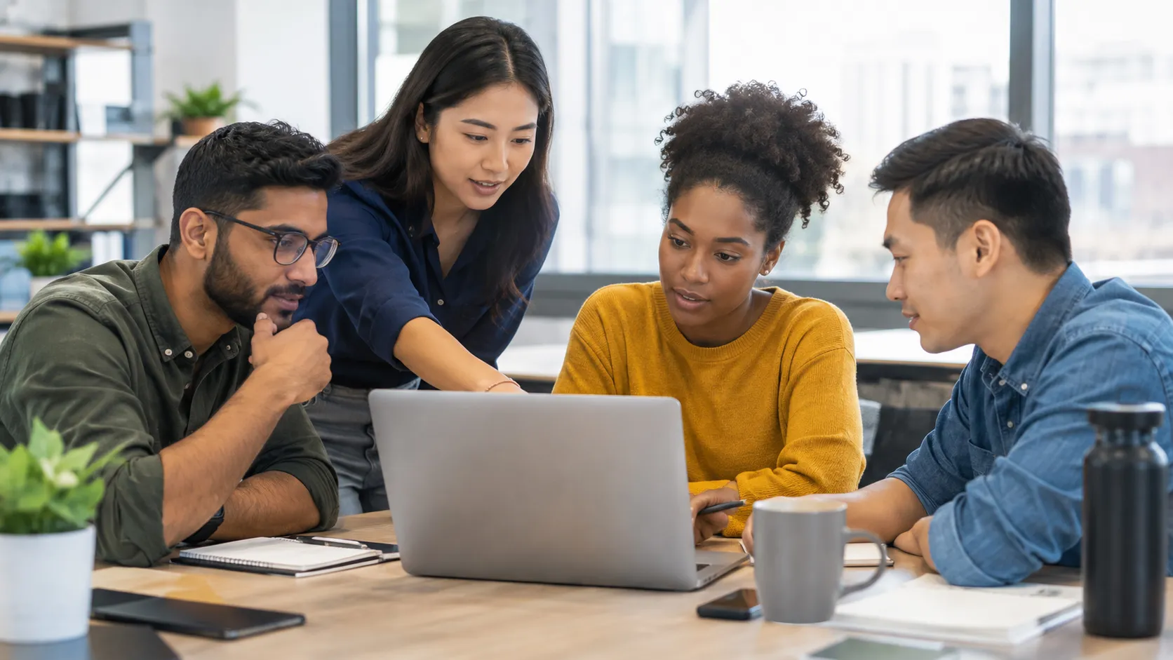 A team of young professionals collaborates around a laptop in a modern office, discussing information and solving a problem through clear communication, shared context, and teamwork to support better business decisions.
